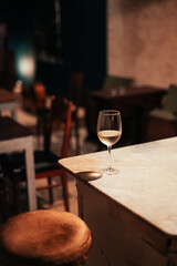 A glass of white wine on a marble table in a dark bar