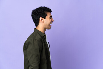 Young Venezuelan man isolated on purple background laughing in lateral position