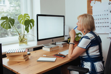 Woman working from home office. Computer with blank empty screen for copy space and information. A...