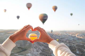 Fototapeta premium Women's hands in the shape of a heart against the background of flying balloons in the sky of Cappadocia. Holidays in Turkey, travel during a pandemic