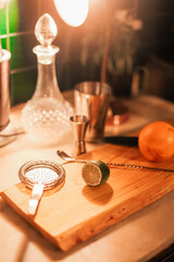 A process of making a cocktail in a bar - orange, lime, cocktail tools on a wooden table with bar light