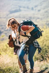 Tuinposter A young couple climbs a mountain, a beautiful day in nature, she carries a backpack for hiking © Sanja