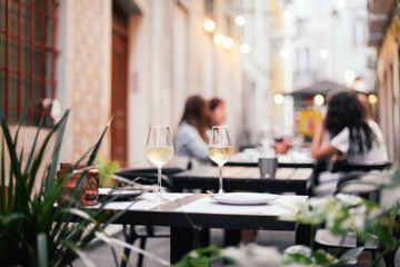 Two glasses of white wine, candles on a served table in an outdoor terrace, romantic dinner date with evening cozy lights