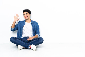 Venezuelan man sitting on the floor saluting with hand with happy expression