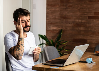 A young man is sitting alone in front of a laptop in the morning, has symptoms of the virus, must...