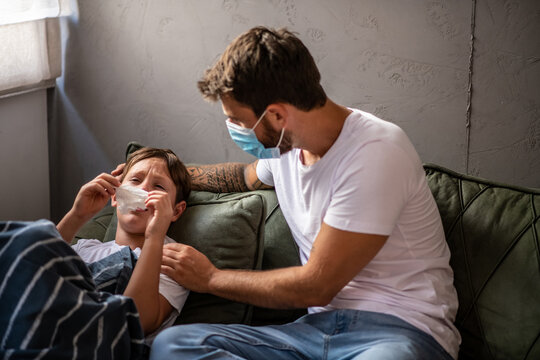The son lies in bed and the father takes care of him, they both put masks on their faces, protection during a pandemic
