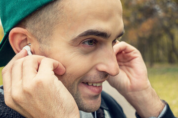 Obraz premium Happy guy listens to music with headphones, man walking in the Park in spring, portrait, closeup