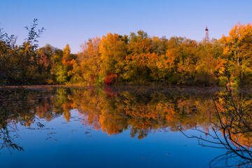 Colorful autumnal photo of a small lake, autumnal small lake with colorful trees in the background, reflections