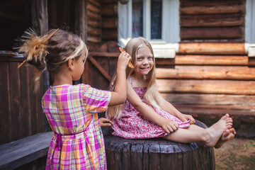 Girl brushing hair of her younger sister on the backyard of wooden house, healthy beauty