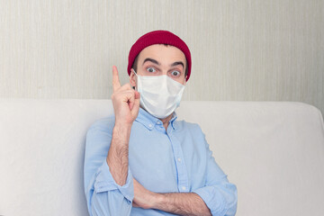 Excited guy in medical mask having good idea and pointing up, portrait. Man at home on...