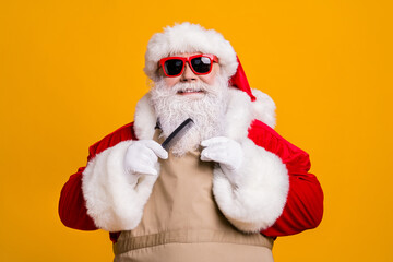Close-up portrait of his he nice attractive cheerful wee-groomed fat grey-haired Santa wearing apron combing beard beauty salon procedure isolated bright vivid shine vibrant yellow color background