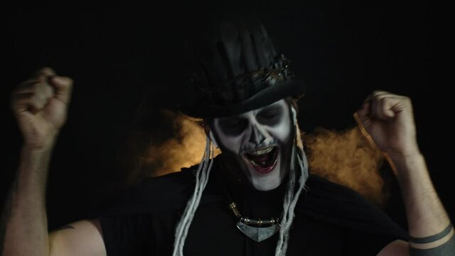 Frightening man in skeleton Halloween cosplay makeup wearing earphones, dancing, celebrating