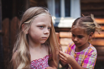 Girl brushing hair of her younger sister on the backyard of wooden house, healthy beauty