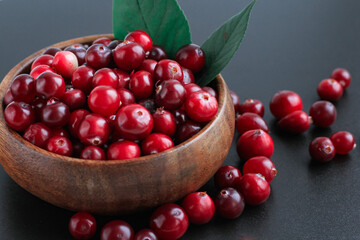 Cranberries in wooden bowl on black background. Nature, autumn, crop, food, berry concept.
