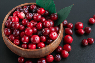 Cranberries in wooden bowl on black background. Nature, autumn, crop, food, berry concept.