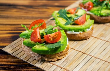 Avocado mash and fresh sliced tomatoes on grilled toast bread on brown wooden background. Trendy and healthy breakfast.