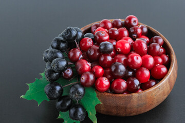 Cranberries and chokeberry in wooden bowl on black background. Nature, autumn, crop, food, berry concept.