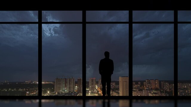 The businessman standing in the office on the night city background. time lapse