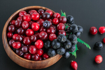 Cranberries and chokeberry in wooden bowl on black background. Nature, autumn, crop, food, berry concept.
