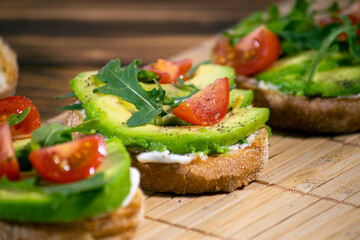 Fototapeta na wymiar Avocado mash and fresh sliced tomatoes on grilled toast bread on brown wooden background. Trendy and healthy breakfast.