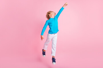 Full length photo of small boy jump raise fist wear blue turtleneck pants sneakers isolated pastel pink color background