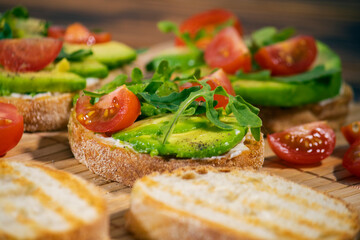 Avocado mash and fresh sliced tomatoes on grilled toast bread on brown wooden background. Trendy and healthy breakfast.