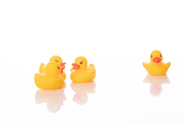 Bullying, gossip concept. One mini yellow rubber duck stands alone while group of ducklings talks about him isolated on white background. Dislike, enmity, distaste, loneliness, hermit. Copy space