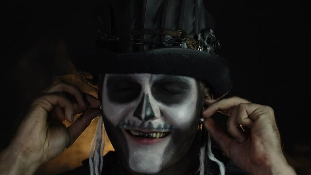 Sinister man with horrible Halloween skeleton makeup puts on headphones, starts dancing, celebrating