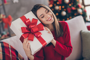 Photo of positive girl sit divan hold big present box wear red sweater in house indoors with x-mas...