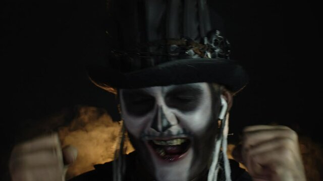 Creepy man with skeleton makeup in top-hat. Guy wearing earphones, listening music, dancing