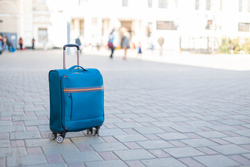 A blue carry-on suitcase stands at the train station.