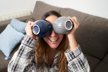 Portrait of woman goofing around at home with 2 cups of coffee.