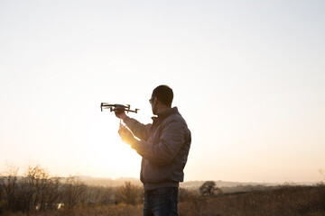 A man launches a drone into the sky. Drone operator with setting sun.