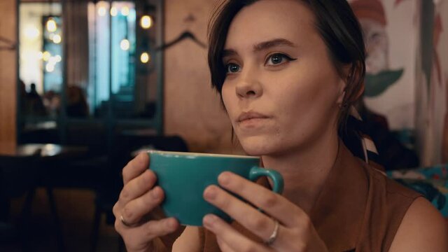 Young woman drinks coffee in cafe. Dreamy girl drinking coffee alone in cozy coffee shop