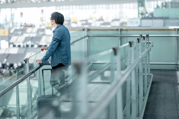 Asian man tourist with suitcase luggage wearing face mask waiting in airport terminal gate hall. Coronavirus (COVID-19) pandemic prevention when travel. Health awareness and social distancing