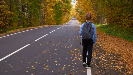 A boy with a school bag walks along the road