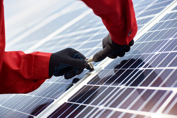 Installing solar panels. Close-up of mans hands in orange uniform and black gloves with wrench in...