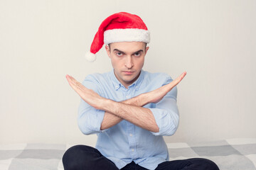Young Santa Claus doing taboo sign, guy is sitting at home on the couch, portrait, white background