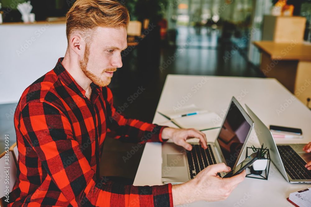 Poster caucasian male programmer sitting at table desk checking received email message on mobile gadget dur