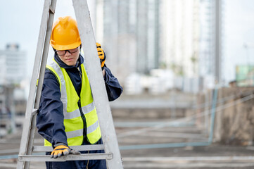 Asian maintenance worker man with safety helmet and reflective suit adjusting aluminium step ladder at construction site. Civil engineering, Architecture builder and building service concepts © zephyr_p
