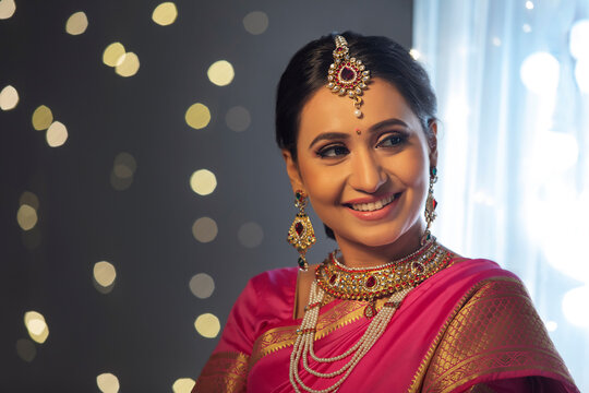 Woman in a pink saree looking sideways with a smile on her face	