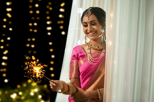 Woman looking at the sparkler in her hand  with a smile on the occasion of Diwali	