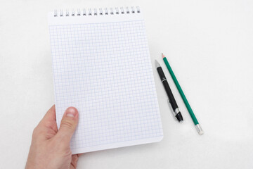 Notepad, pencil, and pen. The human hand shows a spiral notebook, white background, top view, copy space