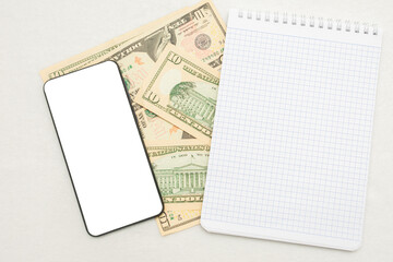 Scattered bills USA dollars, phone and notebook, white background, copy space, top view