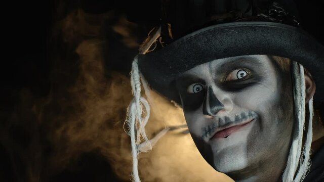 Frightening man in skeleton Halloween makeup turns head and looks into camera with eyes wide open