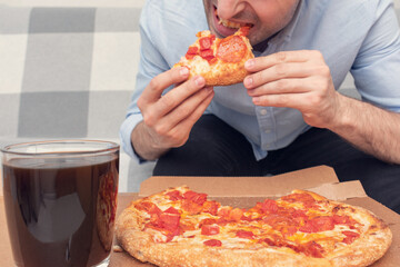 A hungry person bites a slice of pizza, men's hands, cropped image, close-up