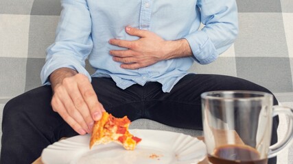 Man with a pizza clutched his stomach, man's hands, cropped image, close-up. The concept of indigestion, 16:9