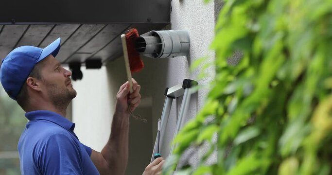 service worker doing maintenance and repair of central gas heating boiler flue chimney on house exterior