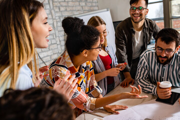 Group of young business people in casual wear discussing architectural designs while sitting in the creative office.