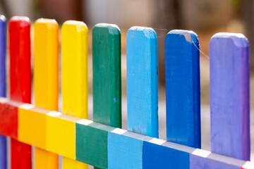 Part of wooden, rainbow colorful painted fence  on a sunny hot summer day in a city park. Abstract multicolored background.